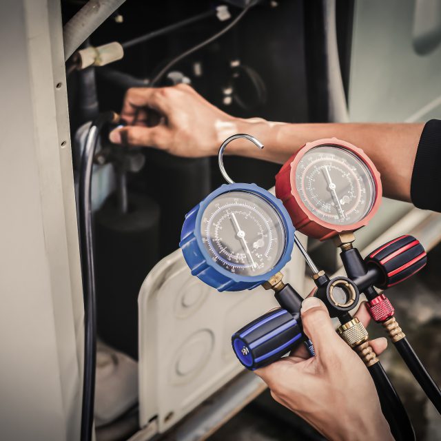 Air repair mechanic using measuring equipment for filling industrial factory air conditioners and checking maintenance outdoor air compressor unit.